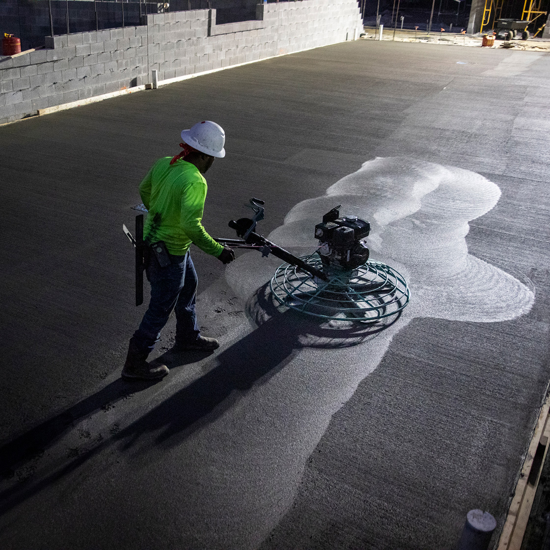 Construction worker finishing job under lights at night; Silverback Concrete.